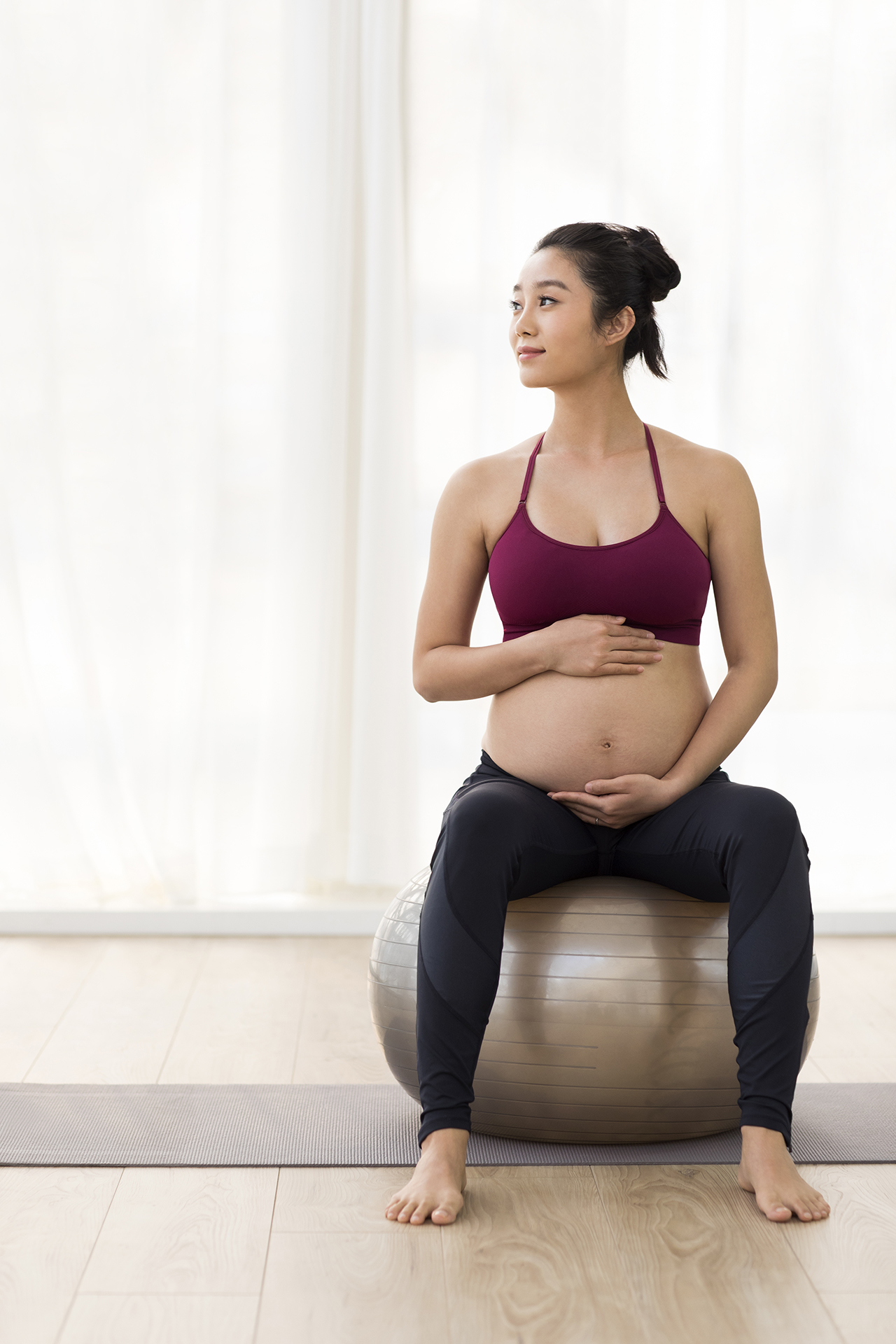Cheerful Chinese pregnant woman sitting on fitness ball Embarazada sentada en una pelota de pilates durante un entrenamiento.